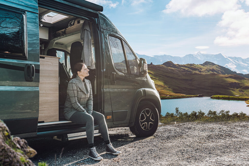 woman sitting in side door of campervan near mountains